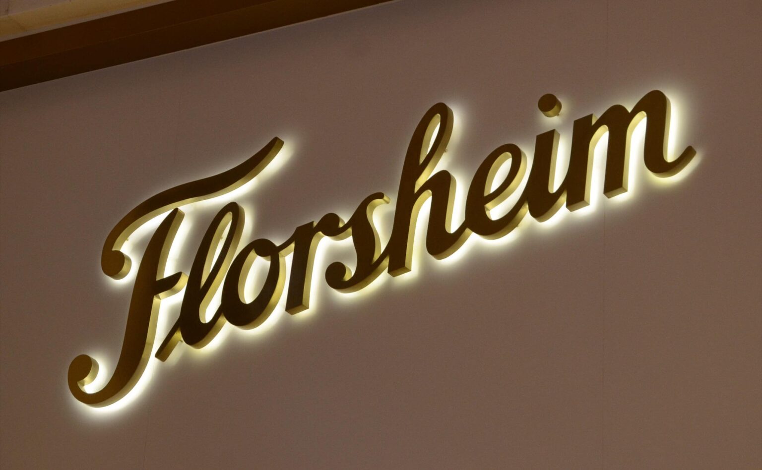 Gold-tone script letters casting a warm halo on a beige wall
