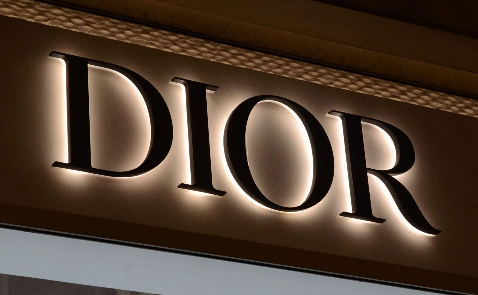 Dark script lettering above a store entrance, ringed by a bright white halo on a beige stone wall